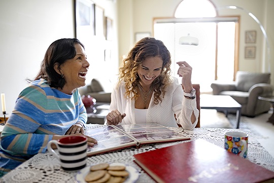 two women looking at a photo album at the dining room table with cookies and coffee, laughing