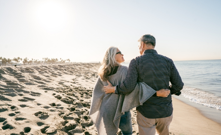 older couple walking down the beach with their arms around each other